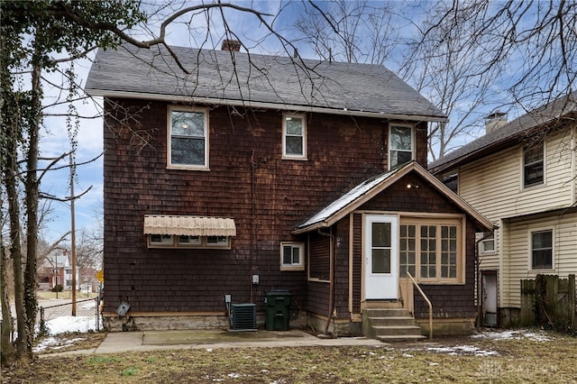 rear view of house featuring entry steps, fence, central AC unit, and roof with shingles