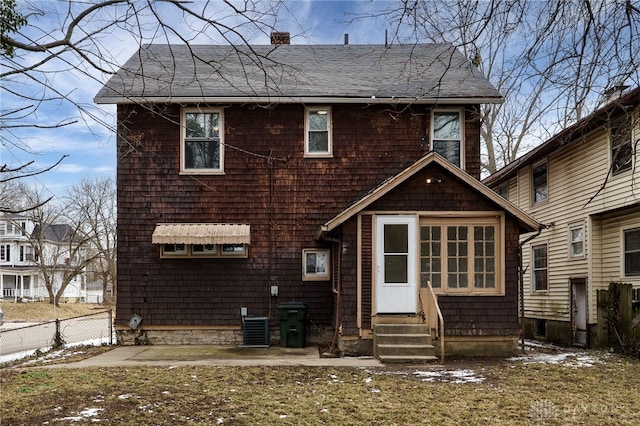 back of property with entry steps, a shingled roof, a chimney, and fence