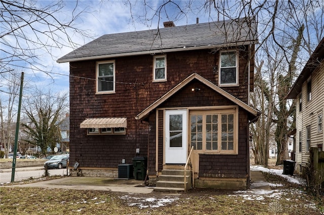 view of front facade featuring a chimney, central air condition unit, a shingled roof, entry steps, and fence