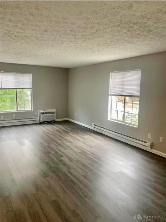 empty room with plenty of natural light, a wall mounted AC, a baseboard radiator, and wood finished floors