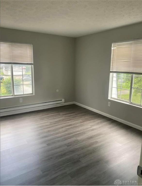 unfurnished room with a textured ceiling, baseboard heating, wood finished floors, and baseboards