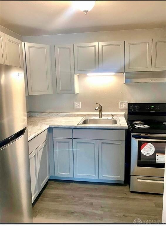 kitchen featuring under cabinet range hood, stainless steel appliances, a sink, light countertops, and light wood-type flooring