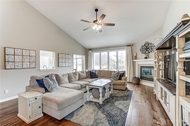 living area with baseboards, dark wood finished floors, ceiling fan, a fireplace, and high vaulted ceiling