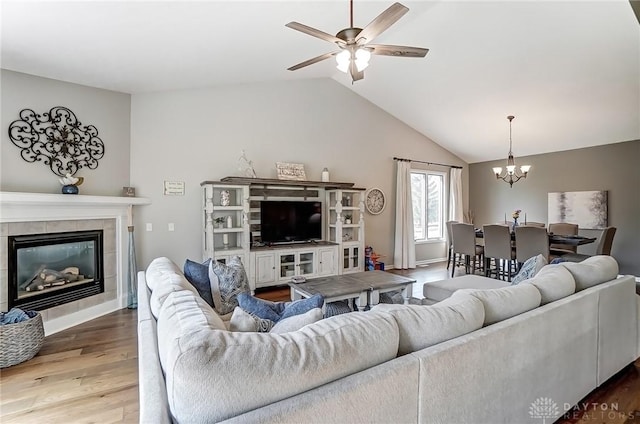 living room featuring baseboards, a tile fireplace, wood finished floors, vaulted ceiling, and ceiling fan with notable chandelier