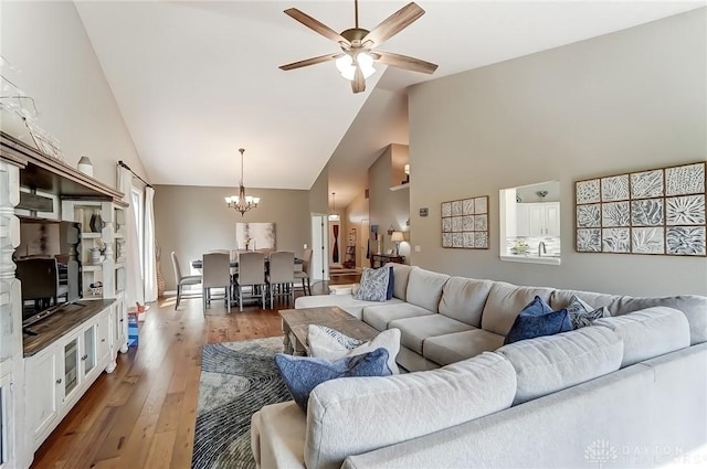 living room with ceiling fan with notable chandelier, high vaulted ceiling, and wood finished floors