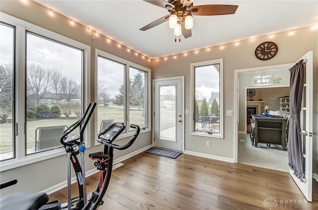 workout area featuring light wood finished floors, ceiling fan, baseboards, and a glass covered fireplace