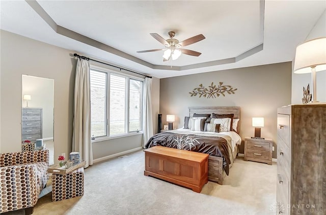 bedroom featuring a tray ceiling, light carpet, ceiling fan, and baseboards