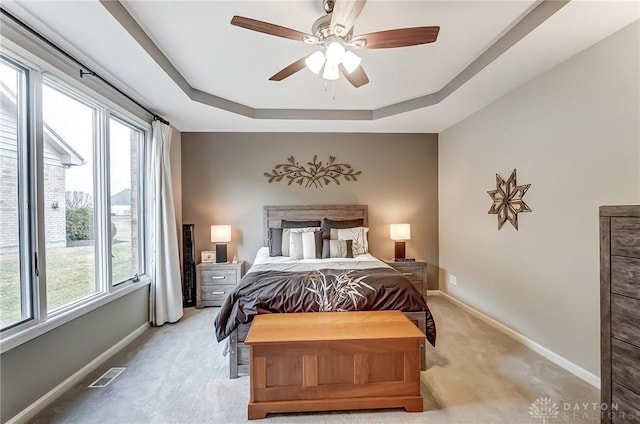 bedroom with baseboards, visible vents, a ceiling fan, light colored carpet, and a tray ceiling