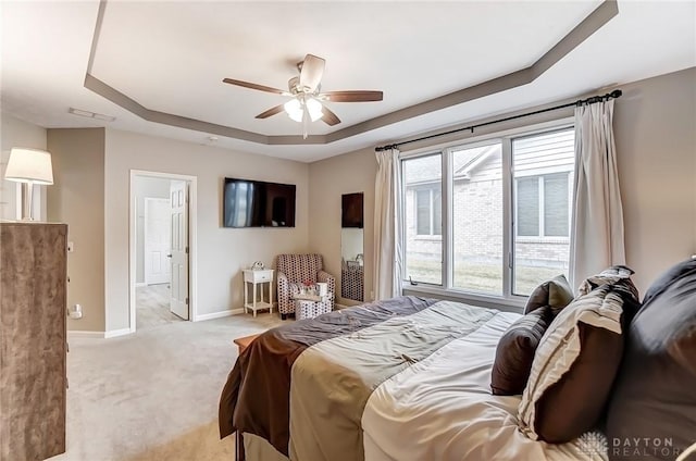 carpeted bedroom with a tray ceiling, a ceiling fan, visible vents, and baseboards