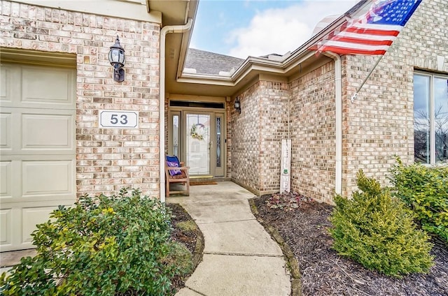 entrance to property with a garage, brick siding, and roof with shingles