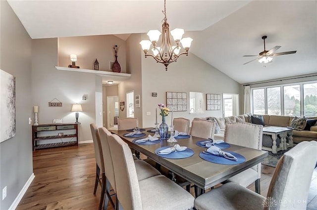 dining area featuring high vaulted ceiling, ceiling fan with notable chandelier, baseboards, and wood finished floors