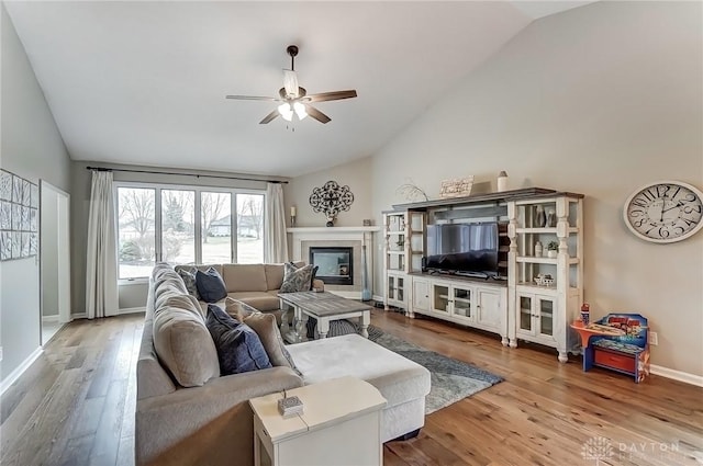 living room with baseboards, a tiled fireplace, a ceiling fan, lofted ceiling, and wood finished floors