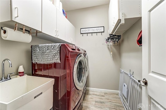 laundry room featuring cabinet space, baseboards, light wood-style flooring, independent washer and dryer, and a sink