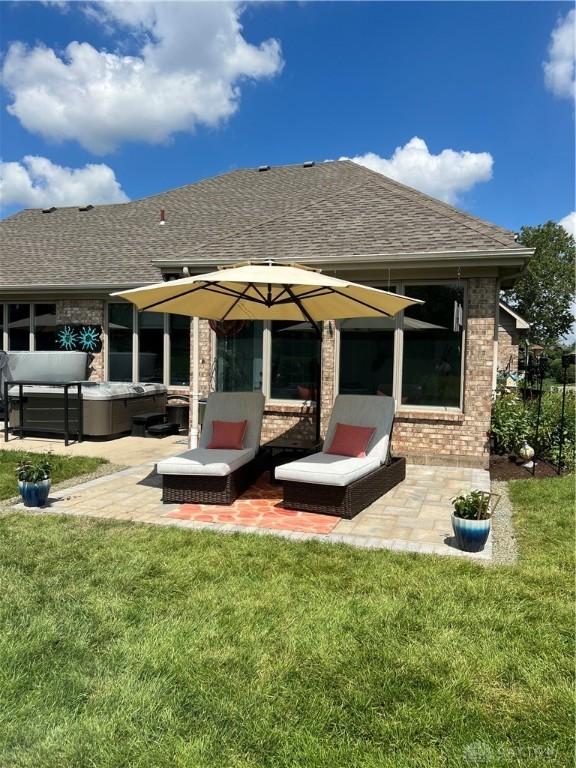 back of property with a yard, brick siding, roof with shingles, and a patio area