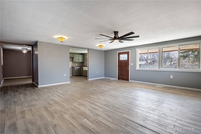 unfurnished living room featuring ceiling fan, a textured ceiling, baseboards, and light wood-style floors