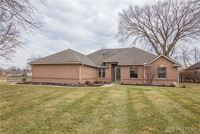 view of front facade with roof with shingles, a front lawn, and brick siding