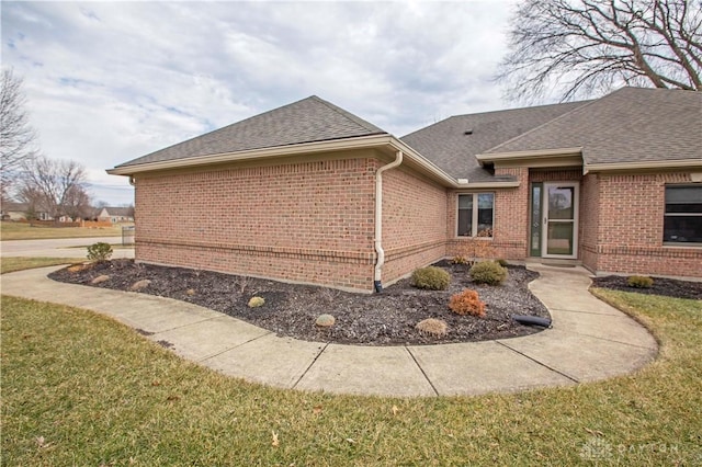 view of side of home featuring roof with shingles, brick siding, and a lawn