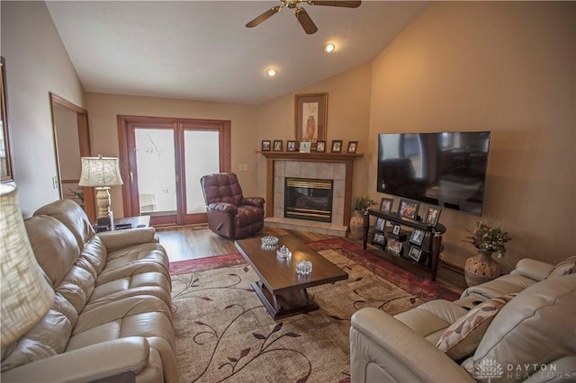 living area with vaulted ceiling, ceiling fan, a tiled fireplace, and wood finished floors