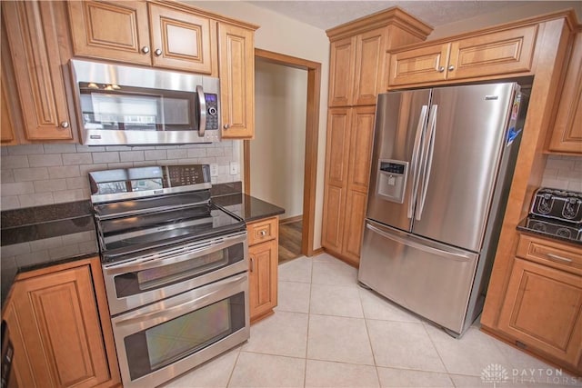 kitchen with light tile patterned floors, appliances with stainless steel finishes, dark stone countertops, and tasteful backsplash