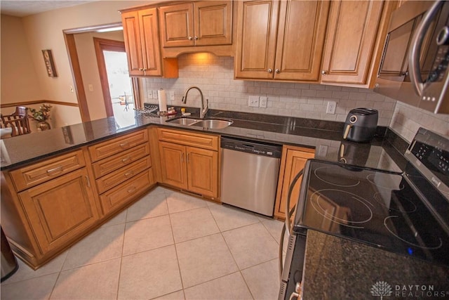 kitchen with light tile patterned floors, stainless steel appliances, backsplash, a sink, and dark stone counters