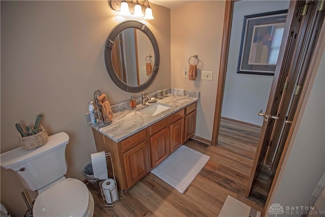 bathroom featuring toilet, baseboards, wood finished floors, and vanity