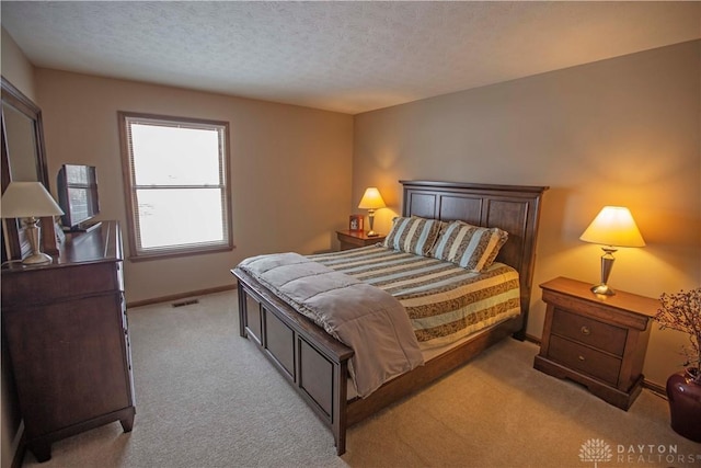 bedroom featuring light carpet, visible vents, baseboards, and a textured ceiling