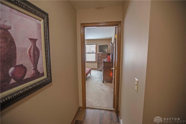 hallway with a textured ceiling, wood finished floors, and baseboards