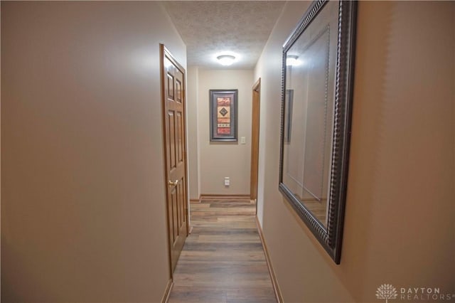 corridor featuring light wood-type flooring, a textured ceiling, and baseboards