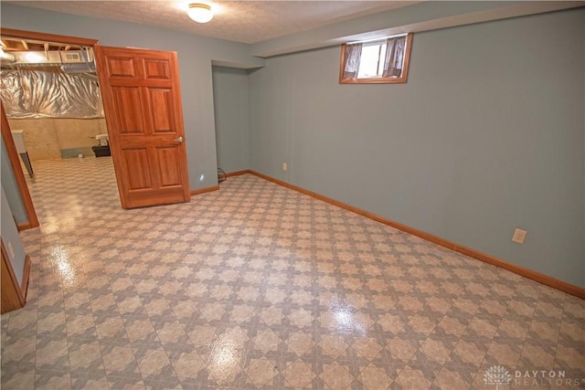 basement with a textured ceiling, baseboards, and tile patterned floors