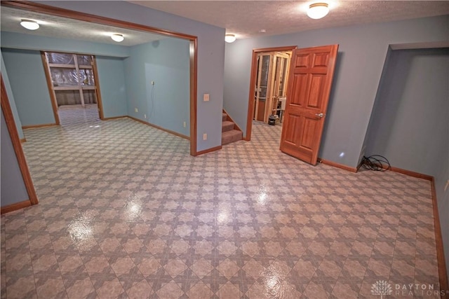 finished basement with a textured ceiling, baseboards, and stairs