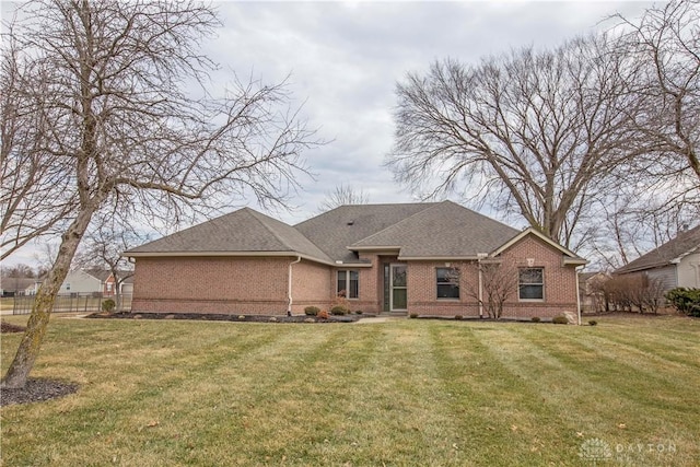 back of house featuring roof with shingles, brick siding, a lawn, and fence