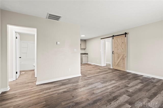 empty room featuring a barn door, wood finished floors, visible vents, and baseboards