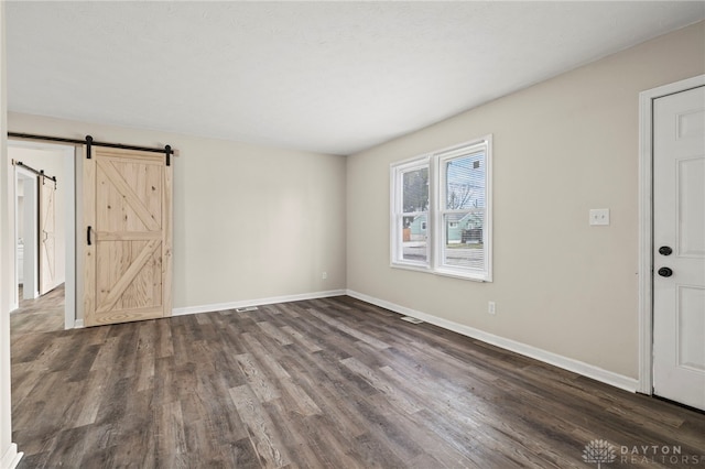 spare room with dark wood-style floors, a barn door, and baseboards