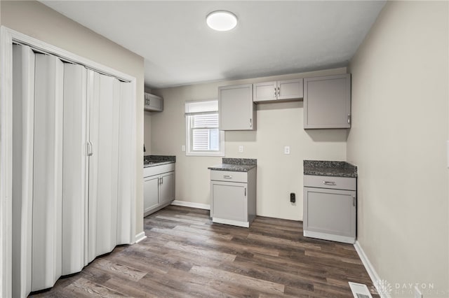 kitchen featuring dark wood-type flooring, visible vents, baseboards, gray cabinets, and dark countertops