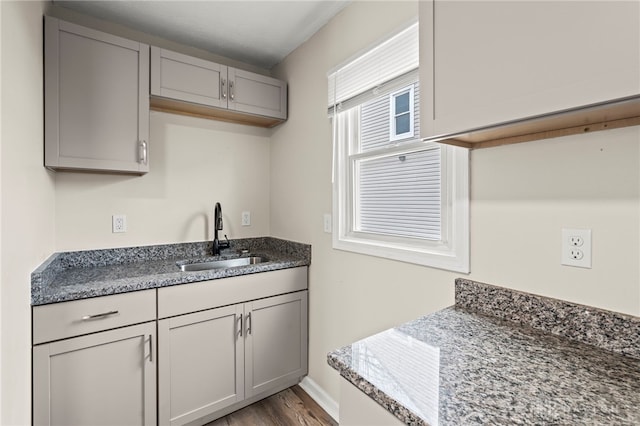 kitchen with gray cabinetry, wood finished floors, a sink, baseboards, and dark stone countertops