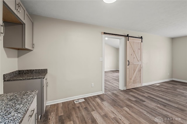 kitchen with a barn door, visible vents, dark wood finished floors, and baseboards