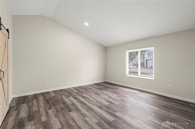 unfurnished bedroom with lofted ceiling, a barn door, dark wood-style floors, and baseboards