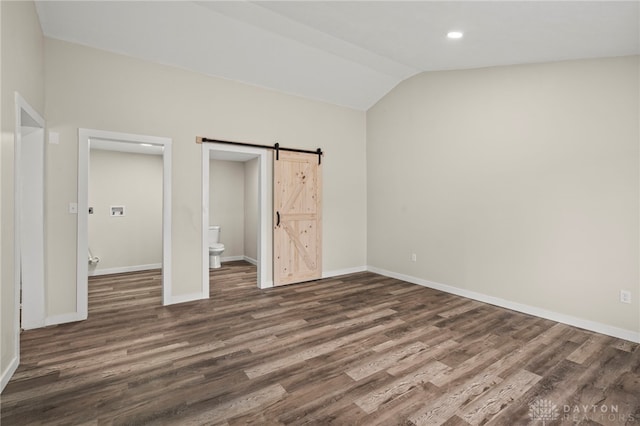 unfurnished bedroom with a barn door, baseboards, vaulted ceiling, dark wood-style floors, and ensuite bath