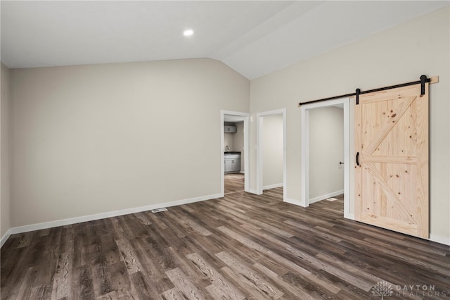 unfurnished bedroom featuring dark wood-style floors, a barn door, baseboards, and vaulted ceiling