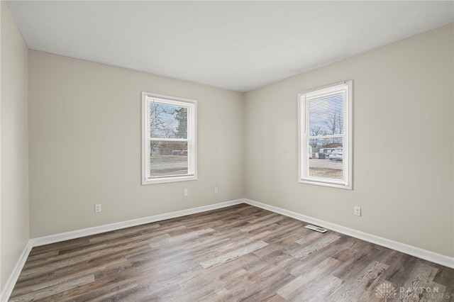 empty room with wood finished floors, visible vents, and baseboards