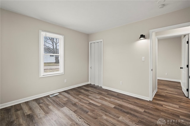 unfurnished bedroom with a closet, dark wood finished floors, visible vents, and baseboards