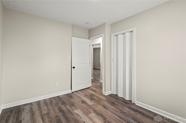 unfurnished bedroom featuring dark wood-type flooring, a closet, and baseboards