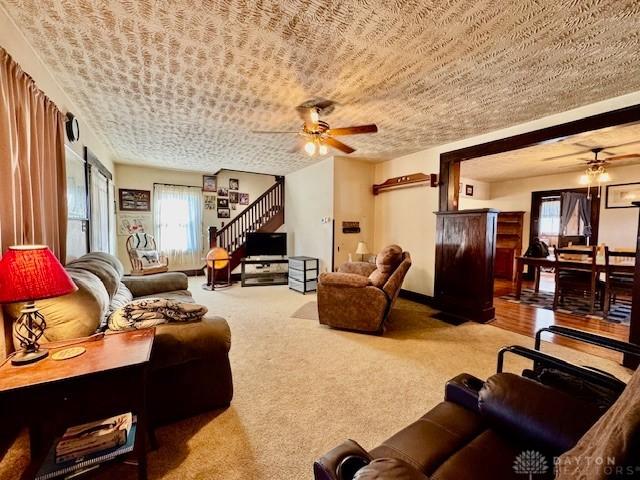 carpeted living room featuring ceiling fan, stairway, and a textured ceiling