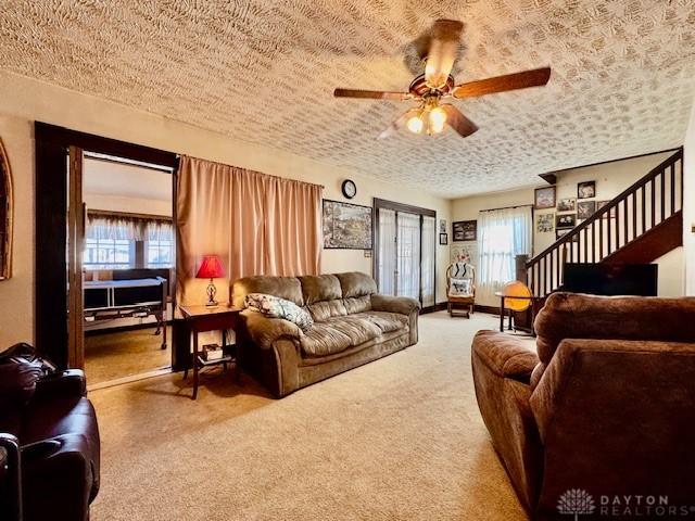 living area featuring carpet floors, ceiling fan, stairs, and a textured ceiling