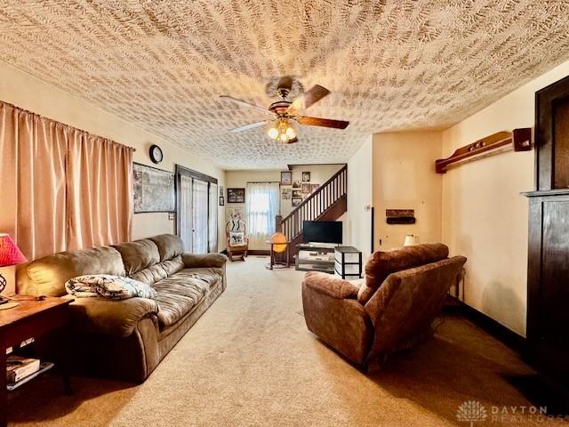 carpeted living area featuring ceiling fan, a textured ceiling, and stairs