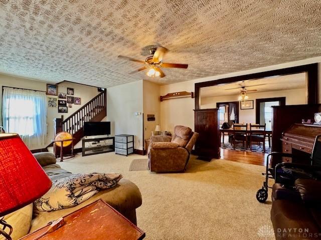 living room featuring carpet, ceiling fan, a textured ceiling, and stairs