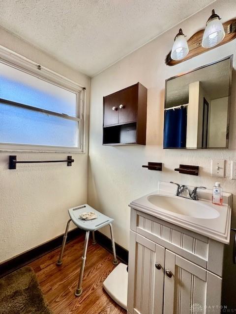 full bath featuring a textured ceiling, wood finished floors, vanity, and baseboards