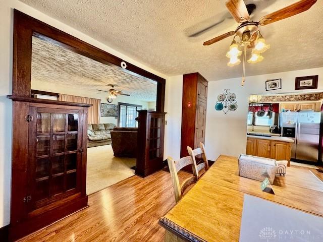 dining space featuring light wood-type flooring, ceiling fan, and a textured ceiling