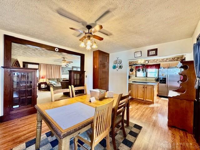 dining area featuring light wood-type flooring, ceiling fan, and a textured ceiling