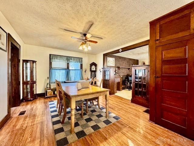 dining room featuring light wood finished floors, a textured ceiling, visible vents, and a ceiling fan